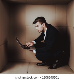 Young Businessman With Laptop In Cardboard Box. Young Man In Suit. Life In Little Cardboard Box. Uncomfortable Life. Personal Spase Concepts. Using Digital Device. Young Introvert.