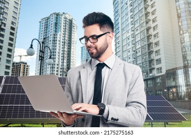 Young businessman with laptop near solar panels and beautiful view of cityscape. Alternative energy source - Powered by Shutterstock