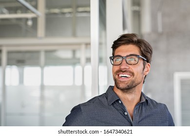 Young Businessman Looking Up With Big Grin. Happy Business Man Wearing Spectacles Looking Away In Office. Close Up Face Of Smiling Guy Having Idea. Man Dreaming Of Success And Pondering New Start Up.