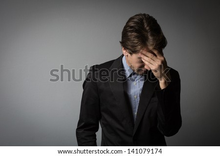 Young businessman looking extremely tired or worried looking down and raising his hand to the foreground