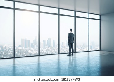 Young Businessman Looking On Window In Contemporary Office With City View.  Workplace And Lifestyle Concept.