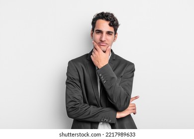 Young Businessman Looking Serious, Thoughtful And Distrustful, With One Arm Crossed And Hand On Chin, Weighting Options