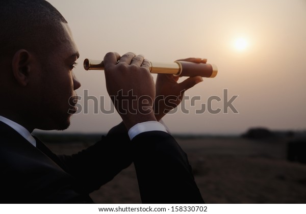 Young businessman looking through telescope in the\
the desert
