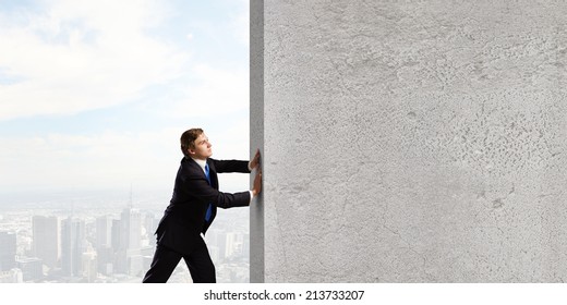 Young businessman making effort to move stone wall - Powered by Shutterstock