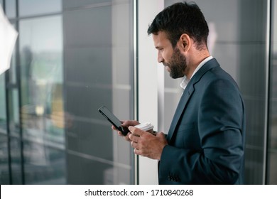 Young businessman in office. Handsome man drinking coffee and using the phone.
