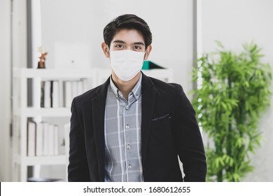 Young businessman in office wearing surgical hygienic protective mask on face standing and looking to camera, idea for prevent crisis of coronavirus and health care for safe of worker and employee. - Powered by Shutterstock