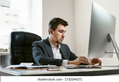 A Young Businessman Or Office Worker At The Workplace Is Typing On A Laptop Keyboard. The Employee Works On A Desktop Computer. Financial Analyst Or IT Specialist, Sales Manager, Freelancer.