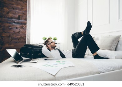 Young businessman on bed working with a laptop from his hotel room - Powered by Shutterstock