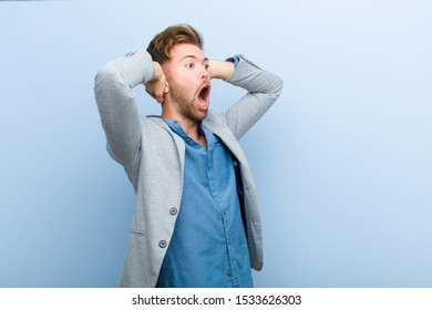 young businessman with open mouth, looking horrified and shocked because of a terrible mistake, raising hands to head against blue background - Shutterstock ID 1533626303
