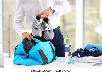 Young Businessman Packing Sports Stuff For Training Into Bag In Office