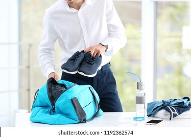 Young Businessman Packing Sports Stuff For Training Into Bag In Office