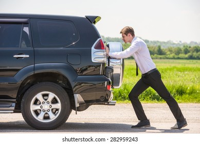 Young Businessman Pushing A Car With Empty Fuel Tank.