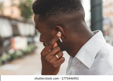 Young businessman put a wireless headphone into the ear. Man will listen audio while walking in the city - Powered by Shutterstock