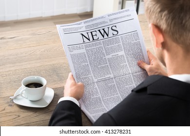 Young Businessman Reading Newspaper At Desk In Office