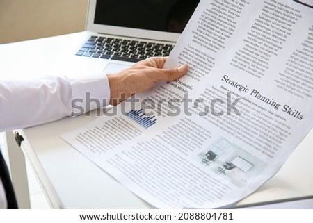 Young businessman reading newspaper in office, closeup