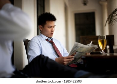 Young businessman reading a newspaper while sitting at a table with his colleague and a glass of beer. - Powered by Shutterstock