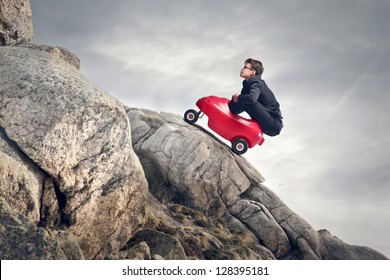 Young Businessman With Red Car Climbs The Rocks