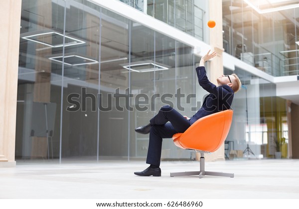 Young businessman relaxing at his chair in modern\
office with stress ball