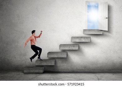 Young businessman running on a staircase leads to an opportunity door to success with bright sunlight