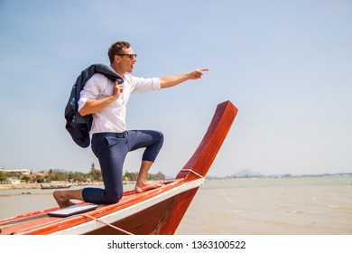 A Young Businessman In A Shirt With A Laptop Sits On A Boat And Points Into The Distance. Full Speed Ahead. Happy Businessman On Vacation.