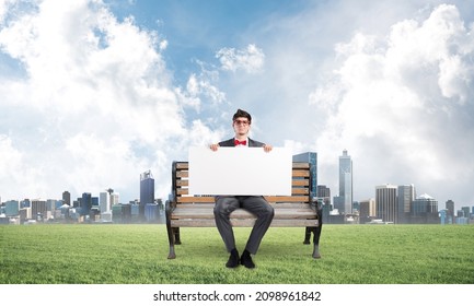 Young businessman sits on a wooden bench and holds a large white banner