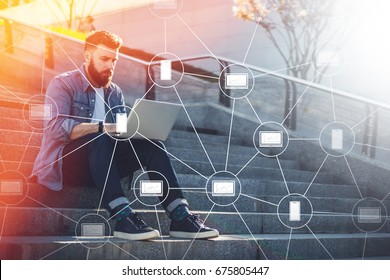 Young businessman sits outdoor on steps, using laptop and looks on his screen.Blockchain technology.Virtual icons.Hipster bearded man is working online,checking email.Student learning online.Lifestyle - Powered by Shutterstock