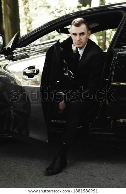 young businessman is sitting in an expensive car and\
looking at the camera. the groom is driving. business man.\
successful guy. rich man.
