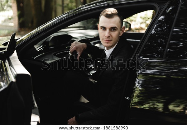 young businessman is sitting in an expensive car and\
looking at the camera. the groom is driving. business man.\
successful guy. rich man.