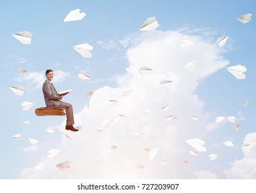 Young businessman sitting on floating in air book with one in hands - Shutterstock ID 727203907