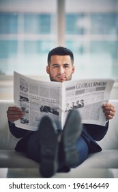 Ein junger Geschäftsmann, der auf Sofa sitzt und Zeitung liest