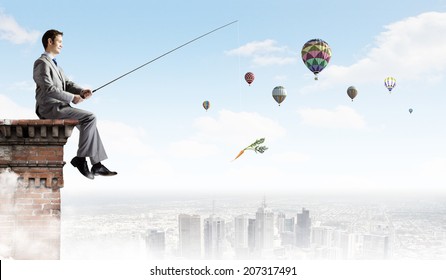Young businessman sitting on top of building and fishing
