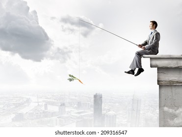 Young Businessman Sitting On Top Of Building And Fishing