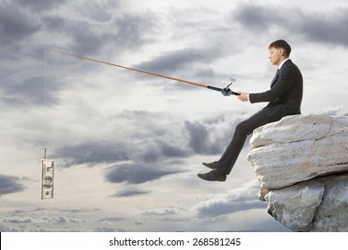 Young businessman sitting on top of rock and fishing
