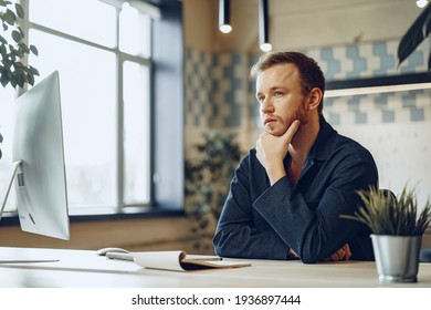 Young businessman sitting at working table in office and pondering something