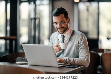 A young businessman in smart casual is drinking coffee and typing on a laptop in cafeteria. - Powered by Shutterstock