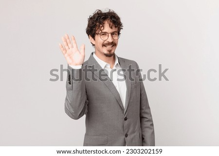 young businessman smiling happily, waving hand, welcoming and greeting you
