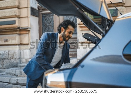 Young businessman smiling while loading his suitcase into the trunk of his car, ready for a business trip or vacation, on a city street with classic architecture