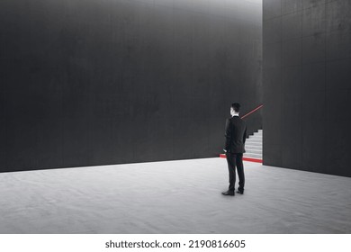 Young Businessman Standing In Creative Dark Concrete Tile Interior With Stairs And Mock Up Place On Wall. School Hallway And Corridor Concept