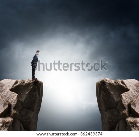 Young businessman standing on edge of rock mountain and looking 