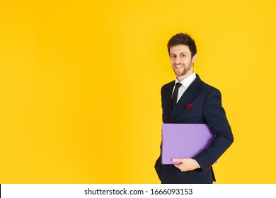 A Young Businessman In A Suit Is Holding A Document File On The Yellow Isolated Background. Business Image For Banners.