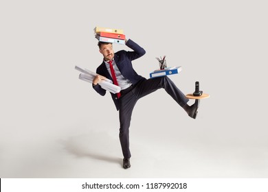 Young businessman in a suit juggling with office supplies in his office, isolated on white background. Conceptual collage with phone, folders. The business, office, work concept.