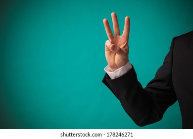 Young Businessman In Suit Showing Hand With Three Fingers Up Over Green Background.