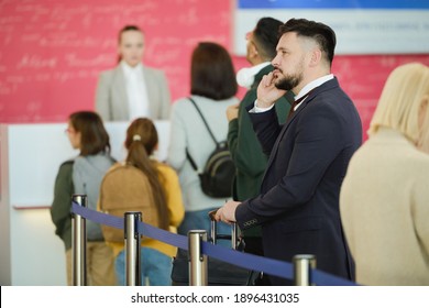 Young Businessman In Suit Talking On Mobile Phone While Standing In A Queue And Waiting For His Registration