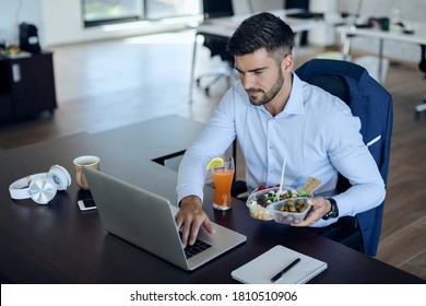 Young businessman surfing the net on computer while eating healthy food in the office.  - Shutterstock ID 1810510906
