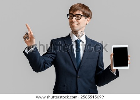 Young businessman with tablet computer using virtual screen on grey background
