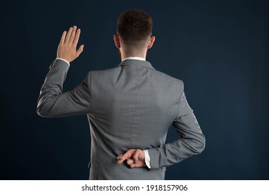 Young businessman taking a fake oath with his back to the camera wearing a grey jacket