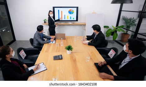 Young Businessman Talking To His Coworkers While Analyzing Charts During A Meeting In Board Room. All Of Them Are Wearing Protective Face Masks Due To COVID-19 Epidemic.