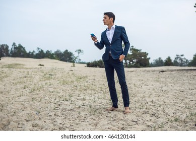 young businessman talking on the phone standing on the sand in the suit