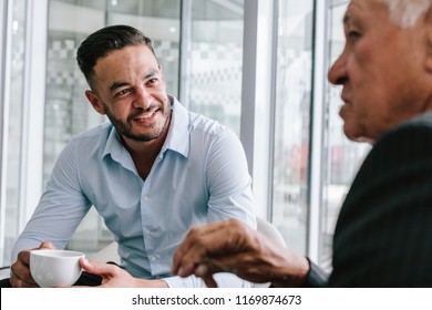 Young Businessman Talking With Senior Man Over A Cup Of Coffee. Business People Having Casual Discussion During Coffee Break.