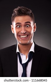 Young businessman with tie undone, making a silly face.Cross eyed young businessman with mouth up to his ears. On black background